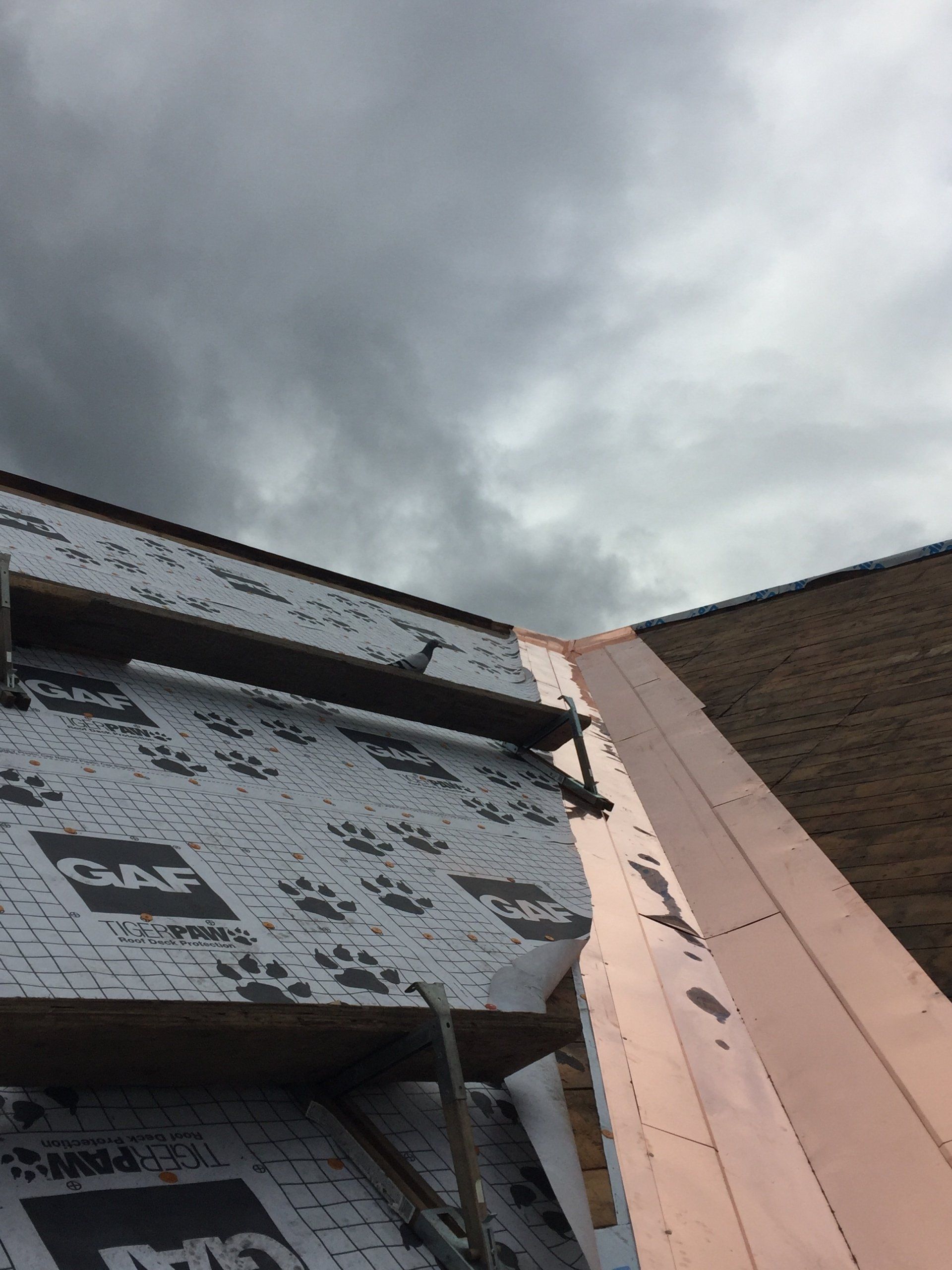 A copper roof is being installed on a building with a cloudy sky in the background.