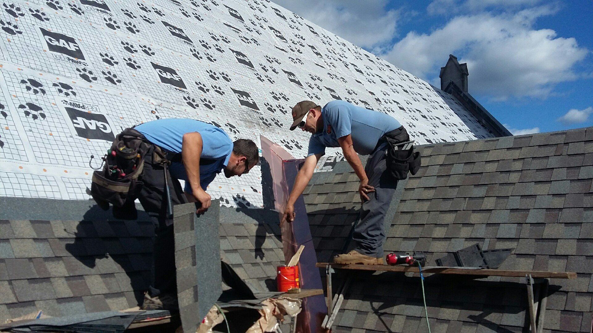 Two roofers installing shingles to a roof.