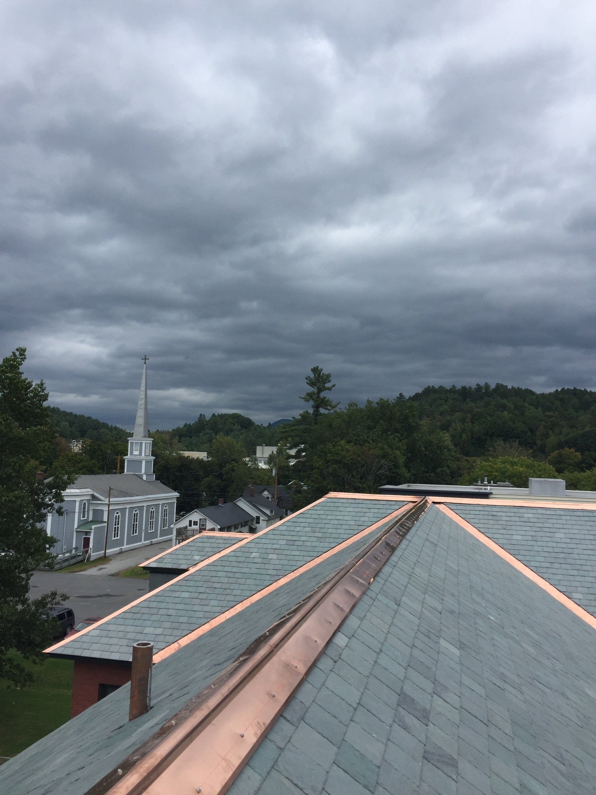 A roof with a copper gutter and a church in the background