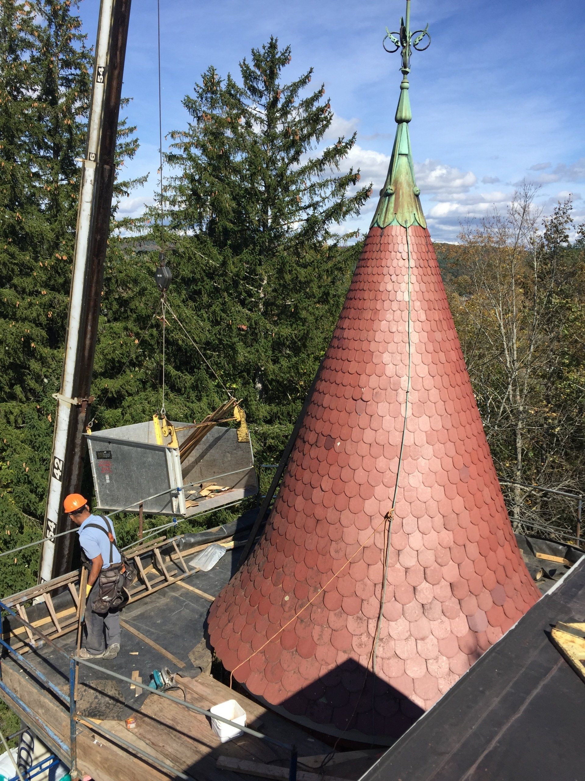 A man is working on the roof of a building with a red cone on top of it.