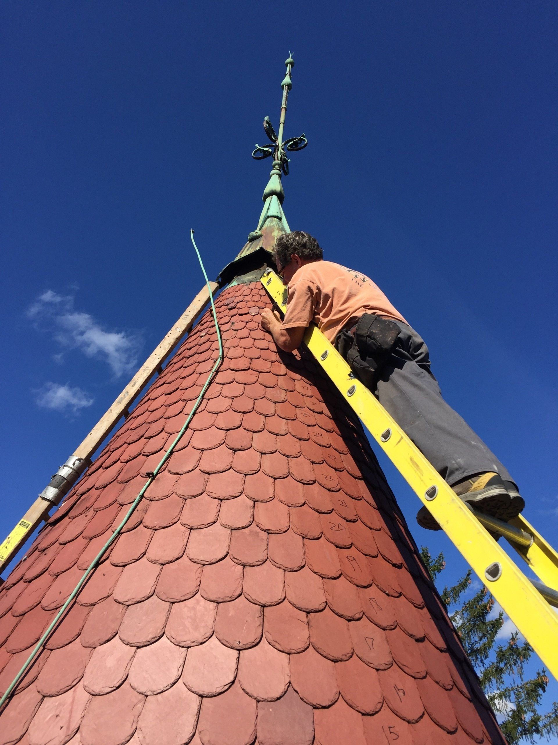A man is standing on a ladder on top of a red roof