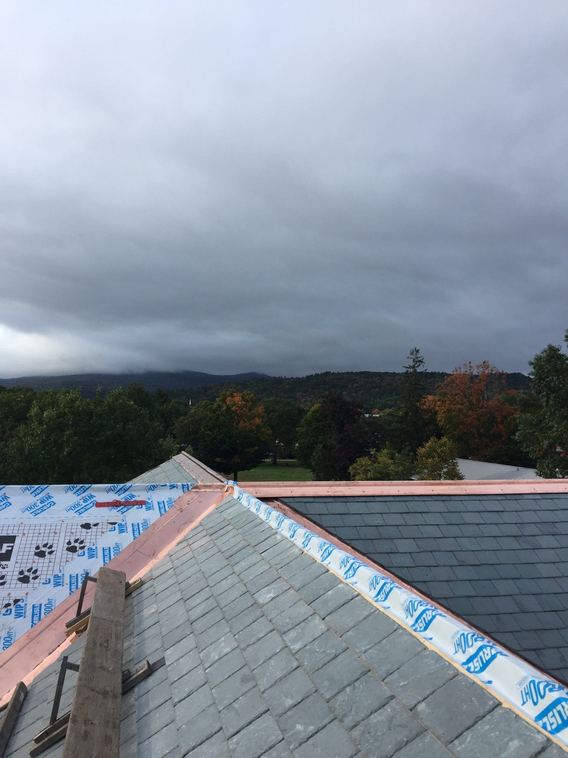 A roof with slate tiles being installed on a cloudy day.