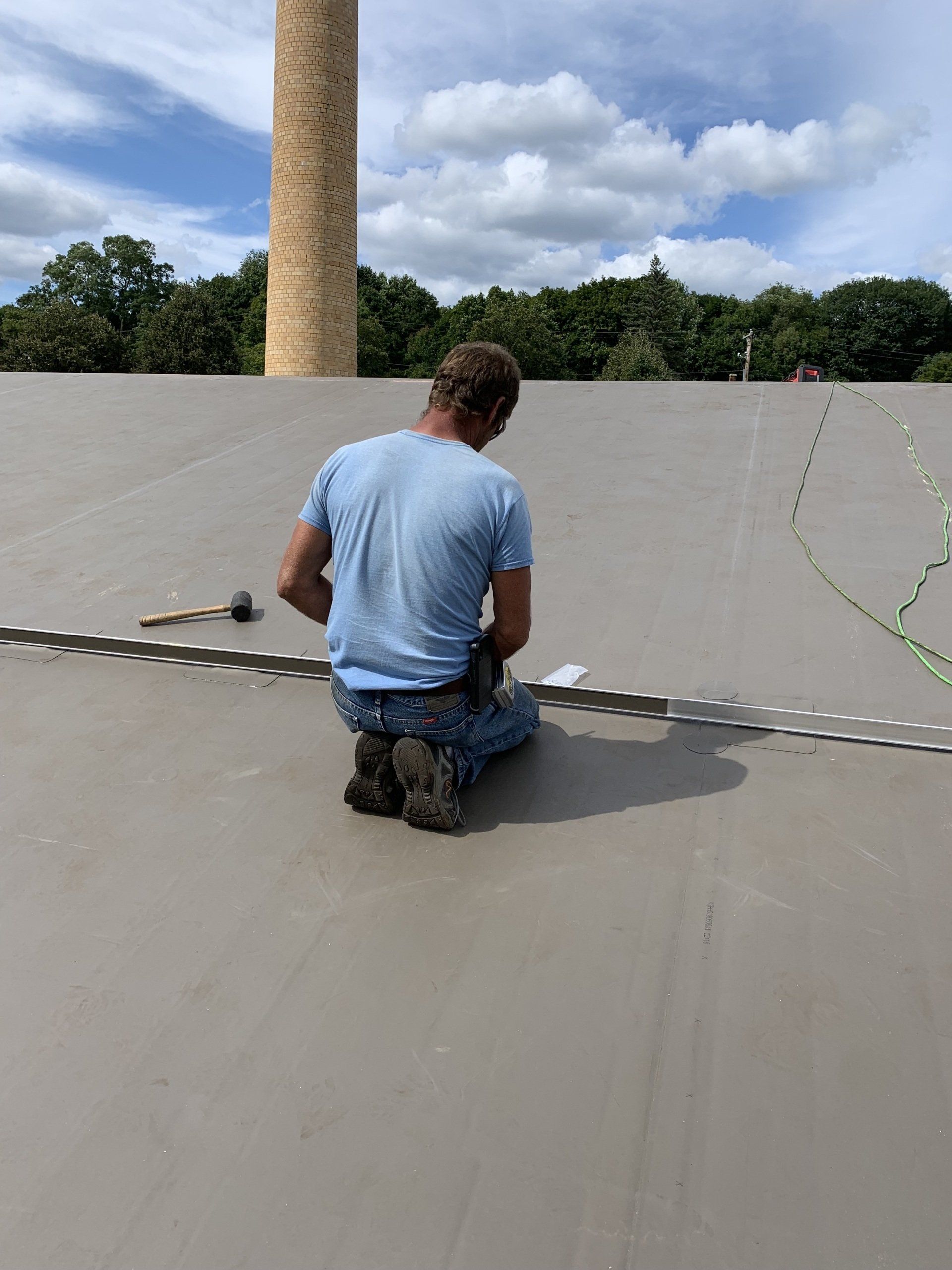 A man is kneeling on the ground working on a roof.