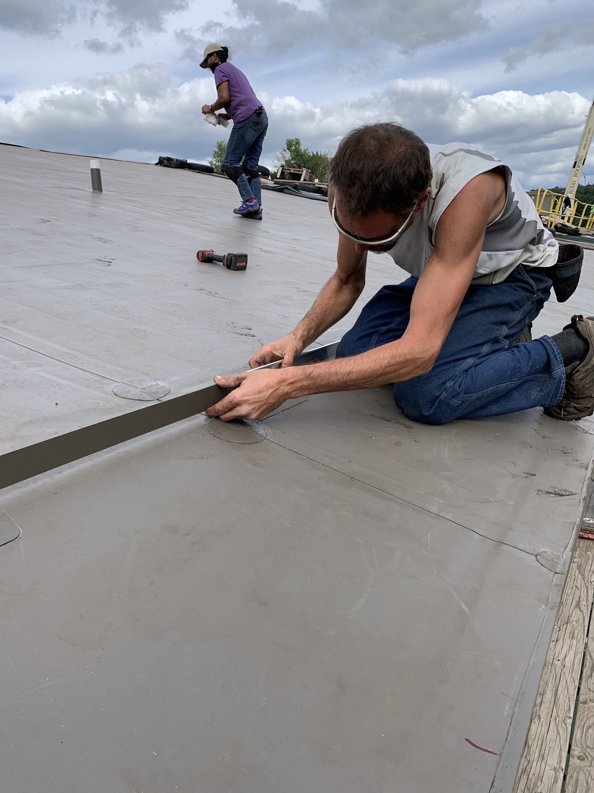 A man is kneeling down on a roof while a woman stands behind him.