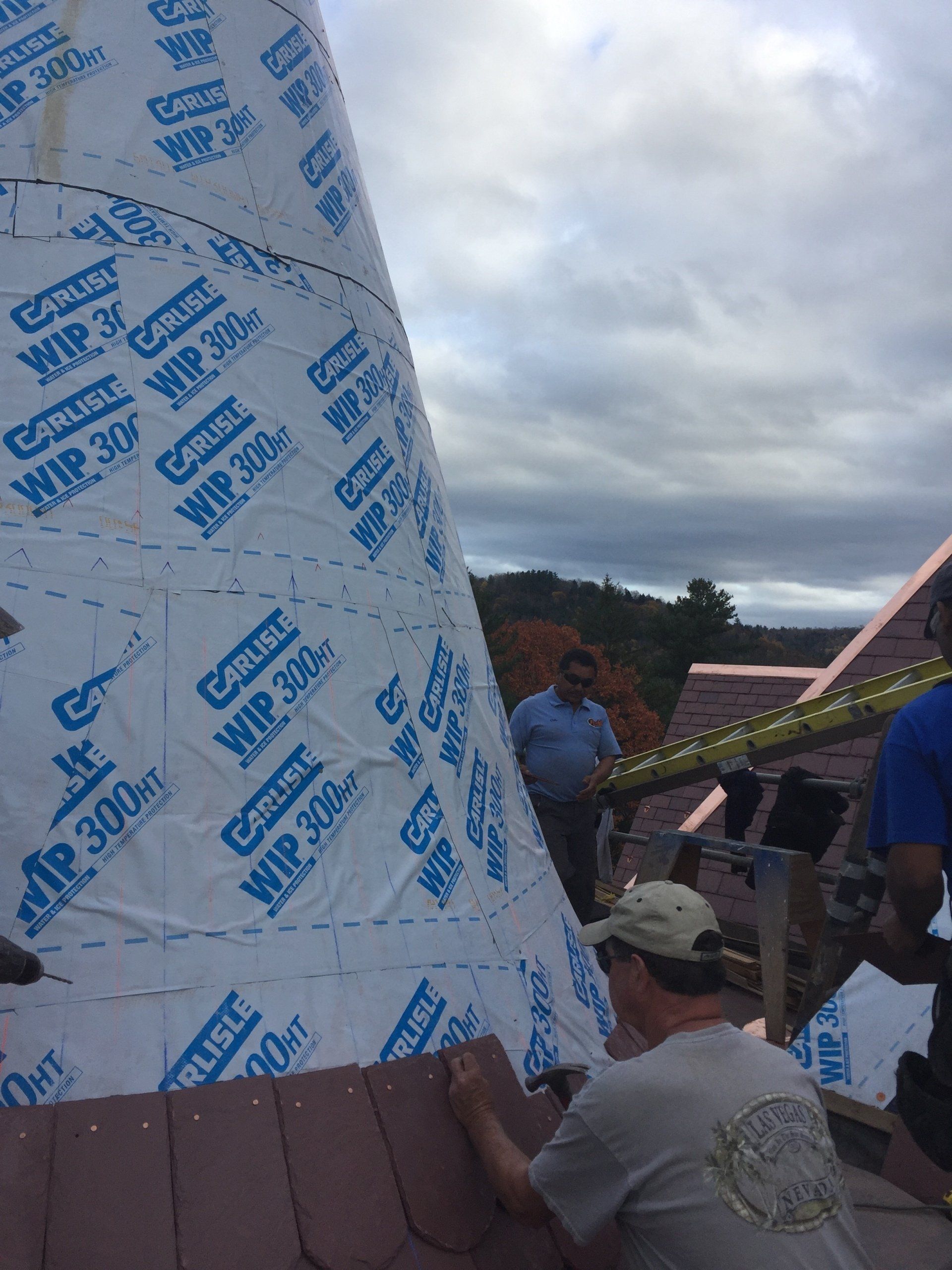 A group of men are working on a roof with a large roll of roofing material.