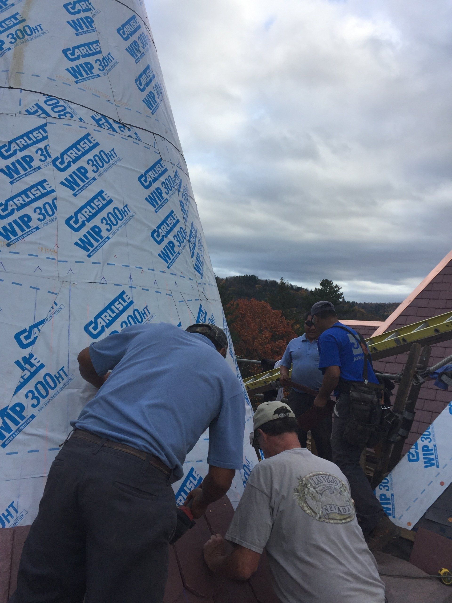 A group of men are working on a roof and one of them is wearing a shirt that says ' nc ' on it