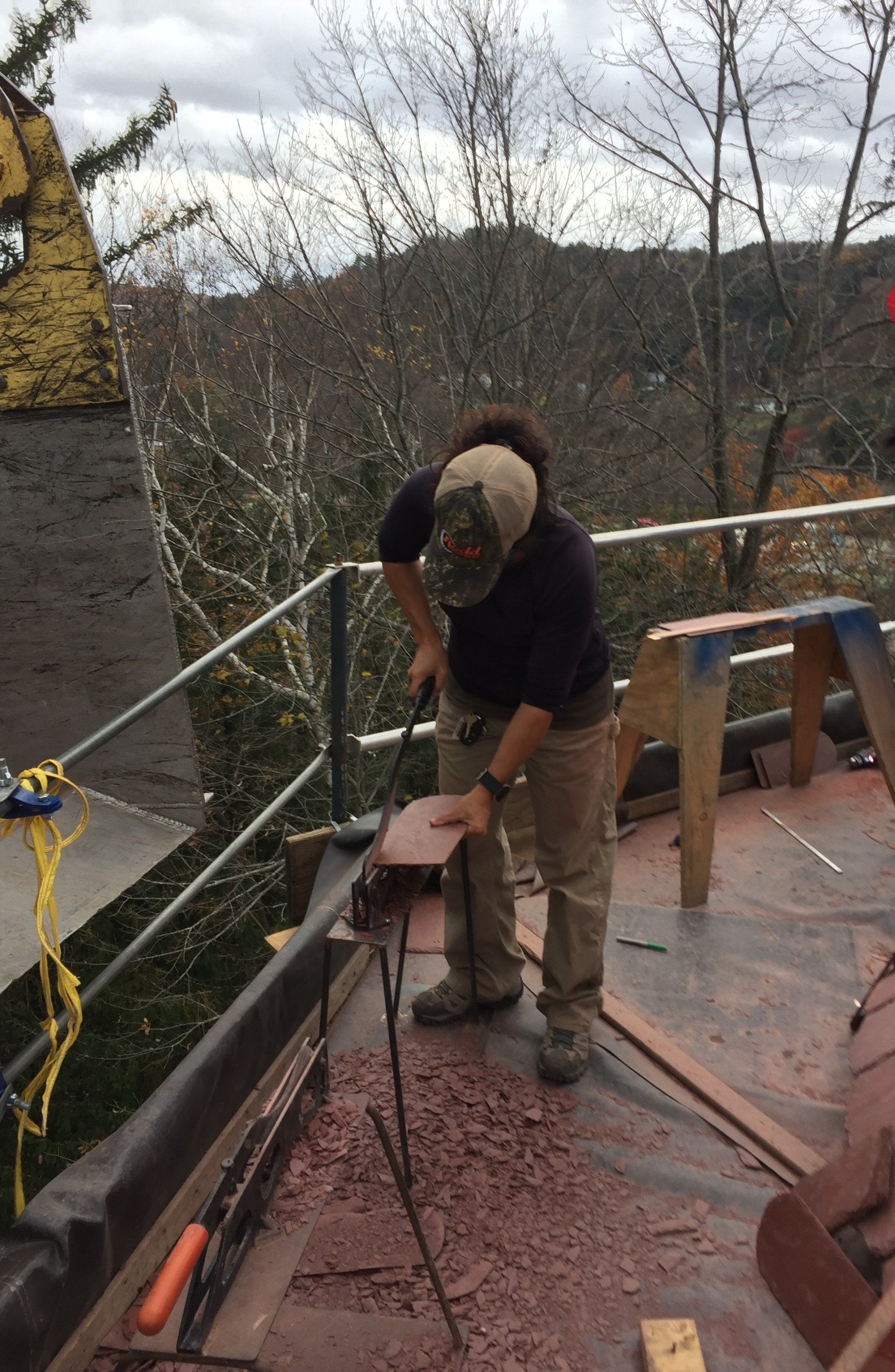 A man is cutting a piece of wood on a roof.