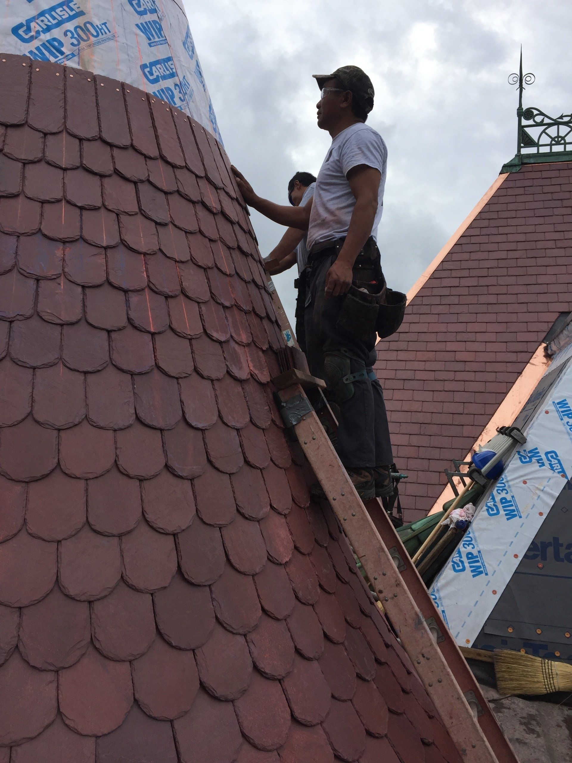 A man is standing on top of a roof with shingles on it.
