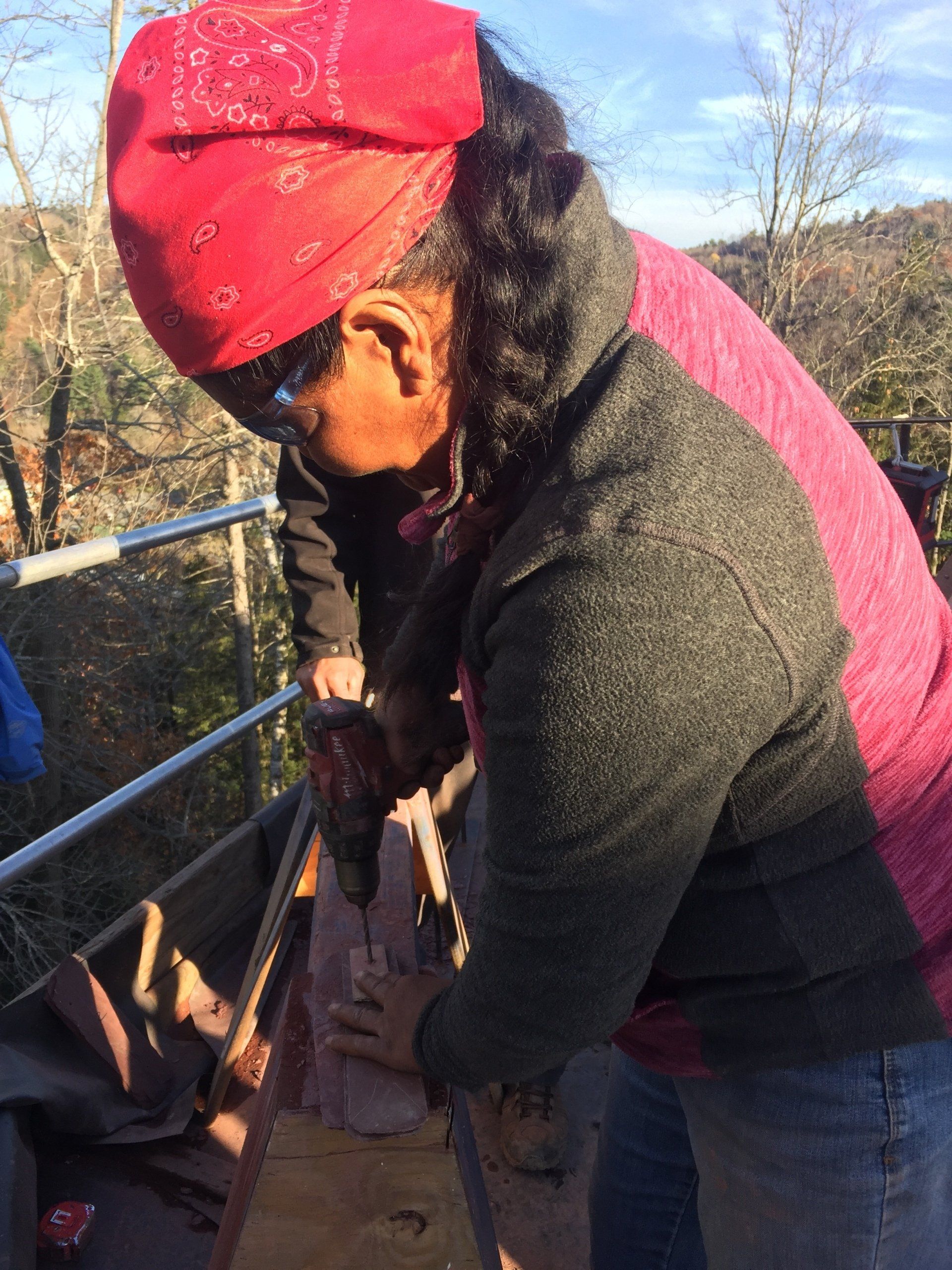 A woman wearing a red bandana is using a drill on a piece of wood.
