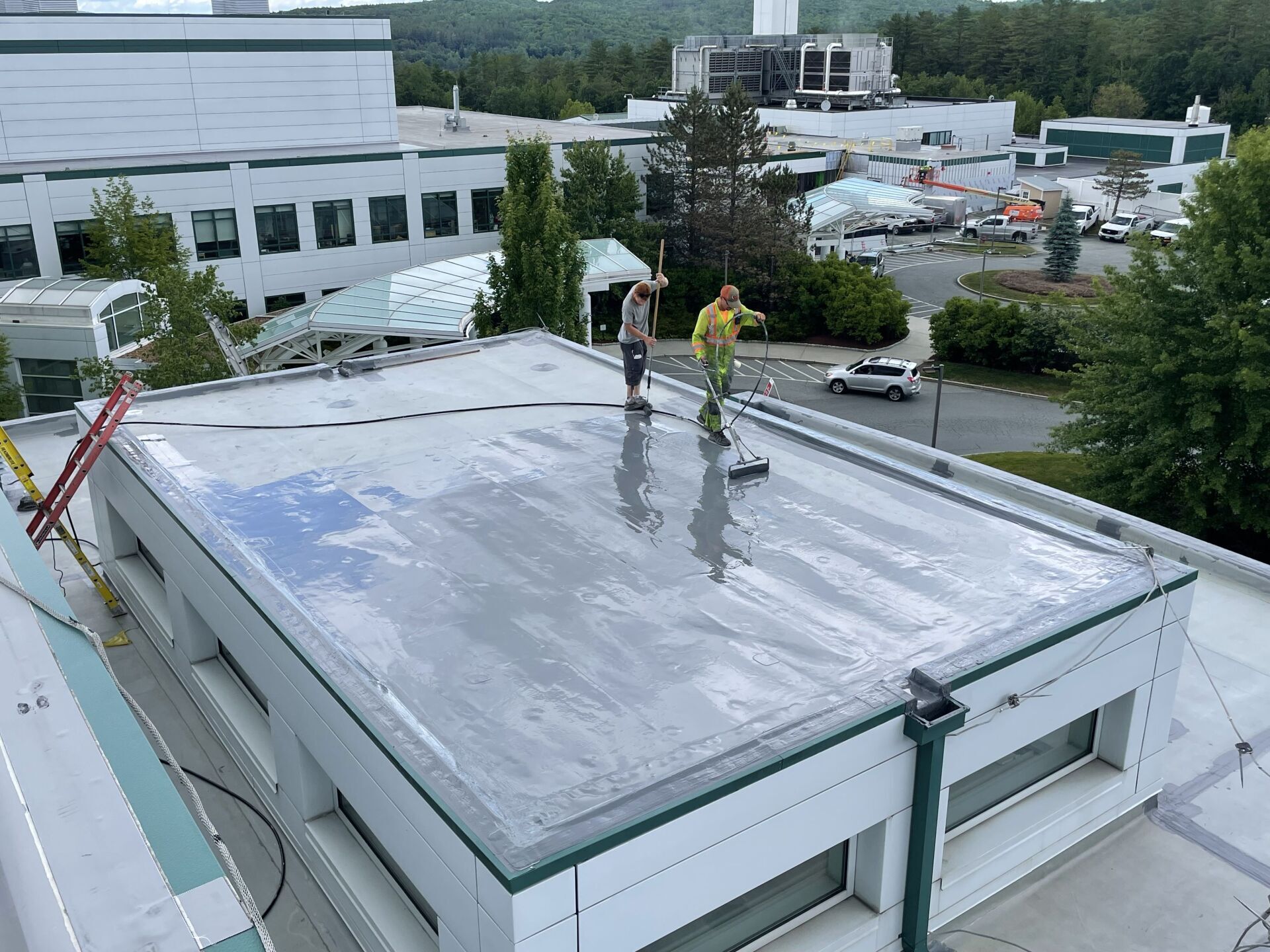 Overhead shot of a commercial building in Vermont with 2 roofers from Rodd Roofing applying a liquid roof coating.