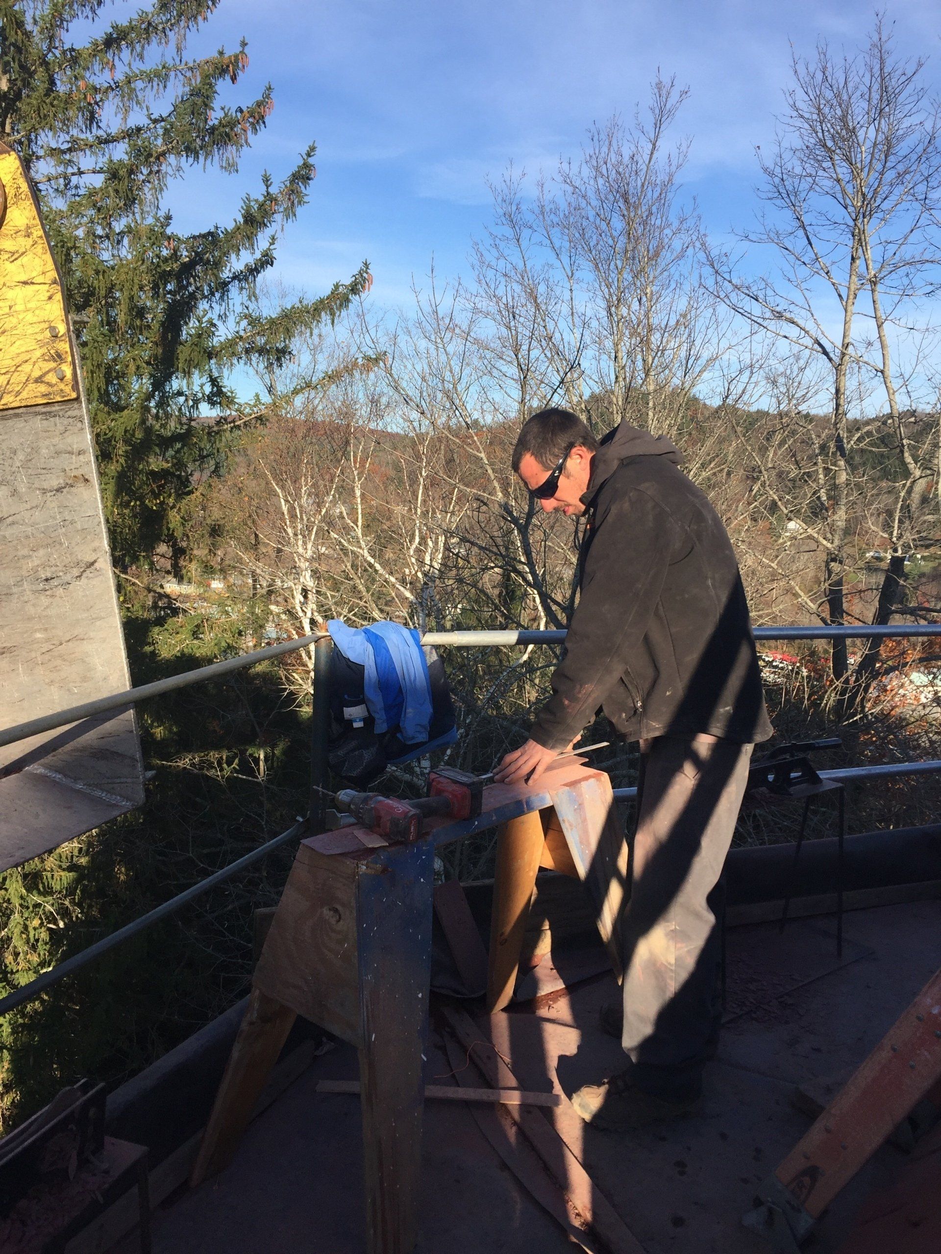 A man in a black jacket is cutting a piece of wood