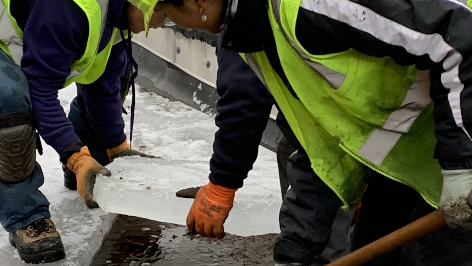 The Rodd Roofing team carefully removes thick layers of ice from the flat roof of a commercial building in Vermont.