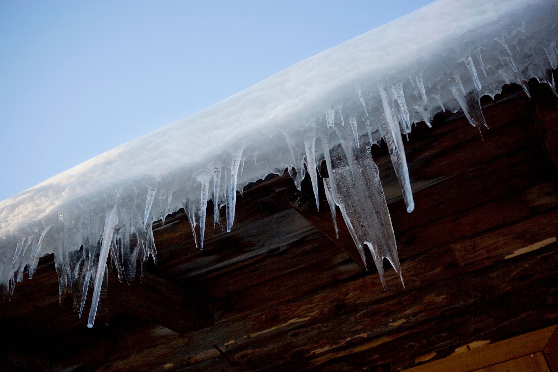 Icicles hanging from a wooden roof against a blue sky.