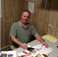 A man is sitting at a desk in a room with wood paneling.