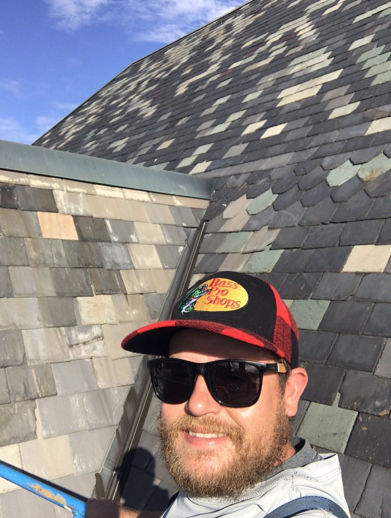 A man wearing a hat and sunglasses is standing on a roof.