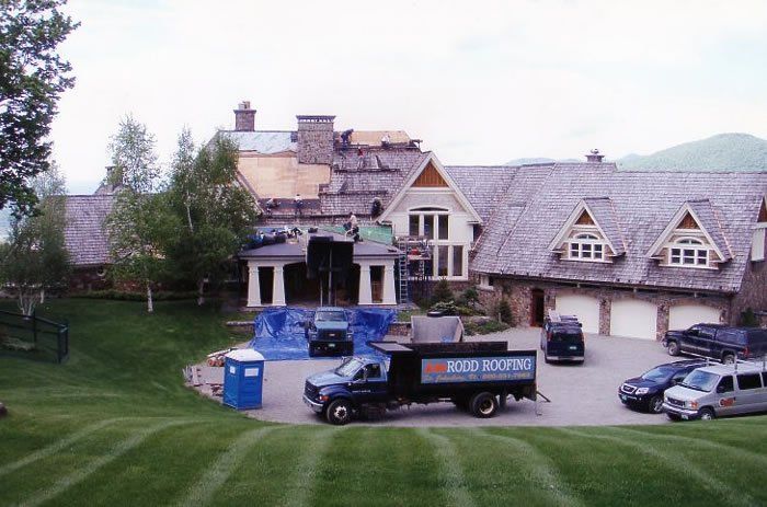 A Rodd Roofing truck is parked in front of a large house with cedar shingles in Vermont