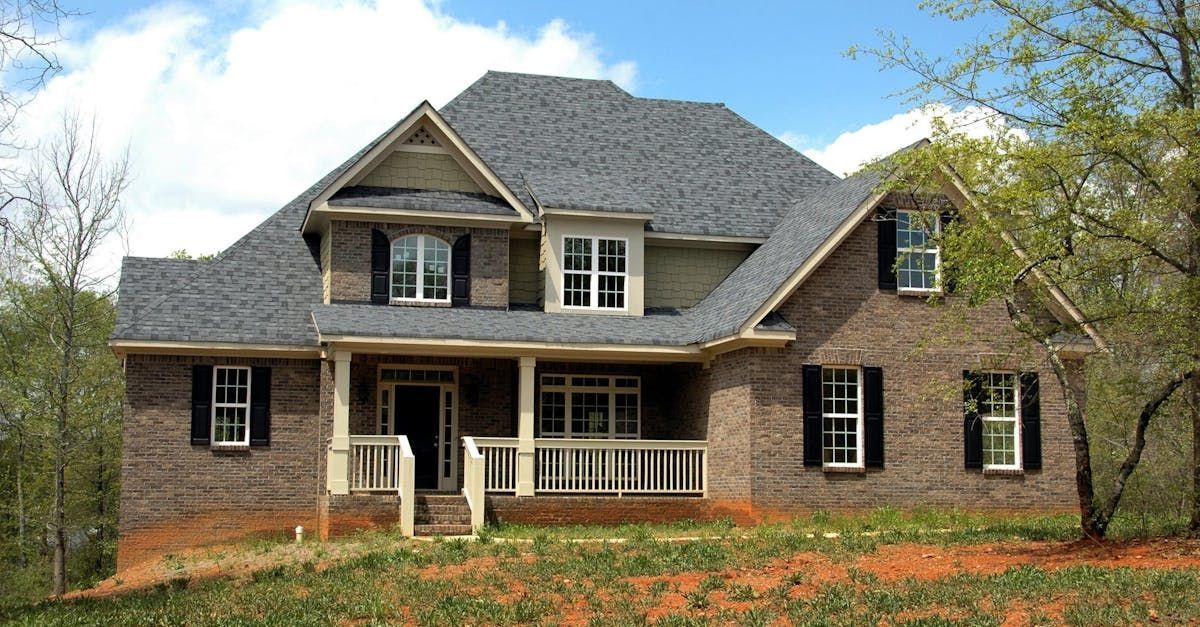 A large brick house in Vermont with a porch, black shutters, and asphalt shingles installed by Rodd Roofing