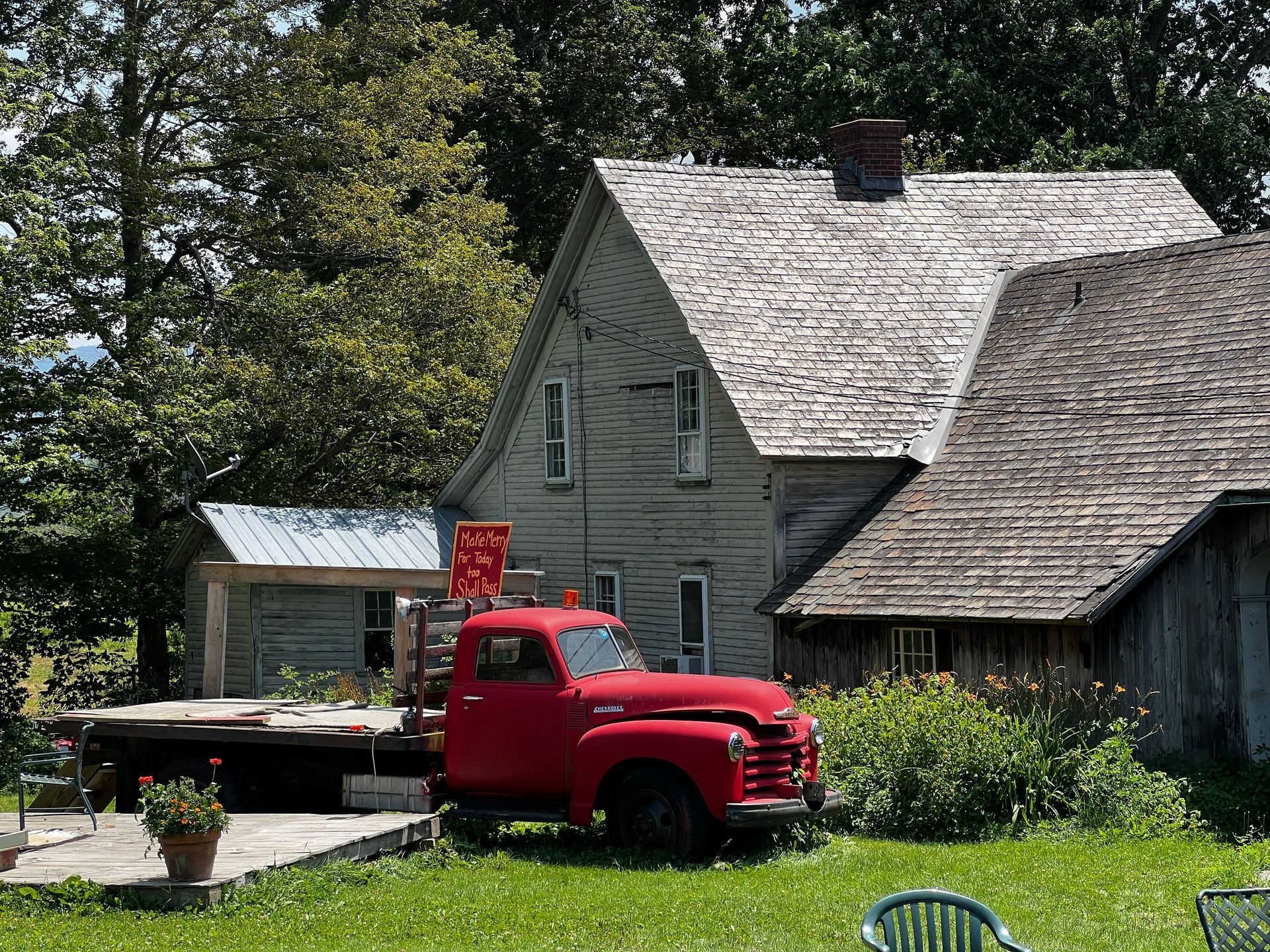 Red vintage truck parked beside a rustic house and covered wagon in a sunny grassy yard