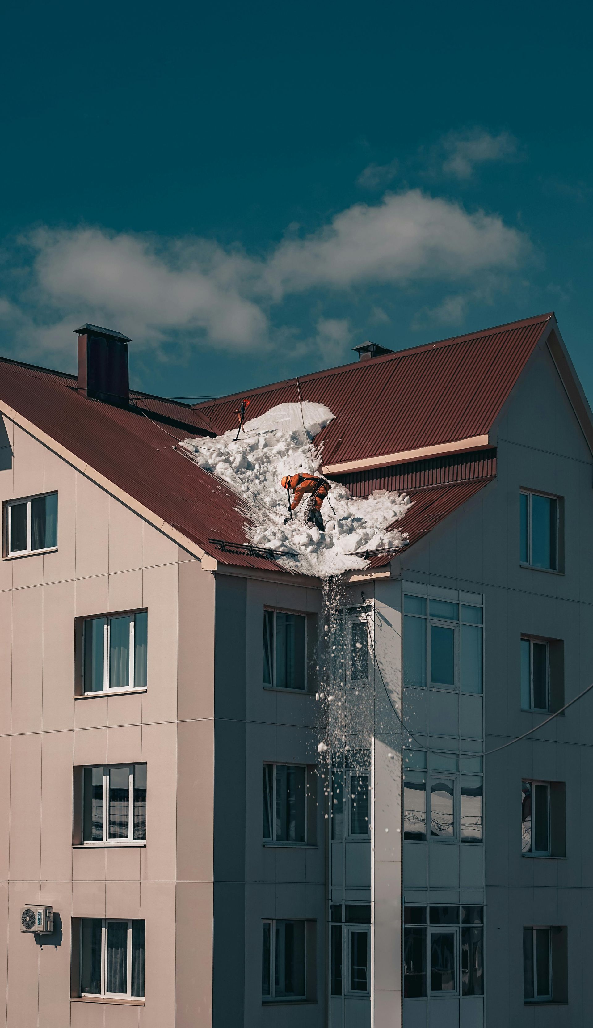 Tall apartment-style building with ice and snow build-up in a roof seam, with man clearing snow off.