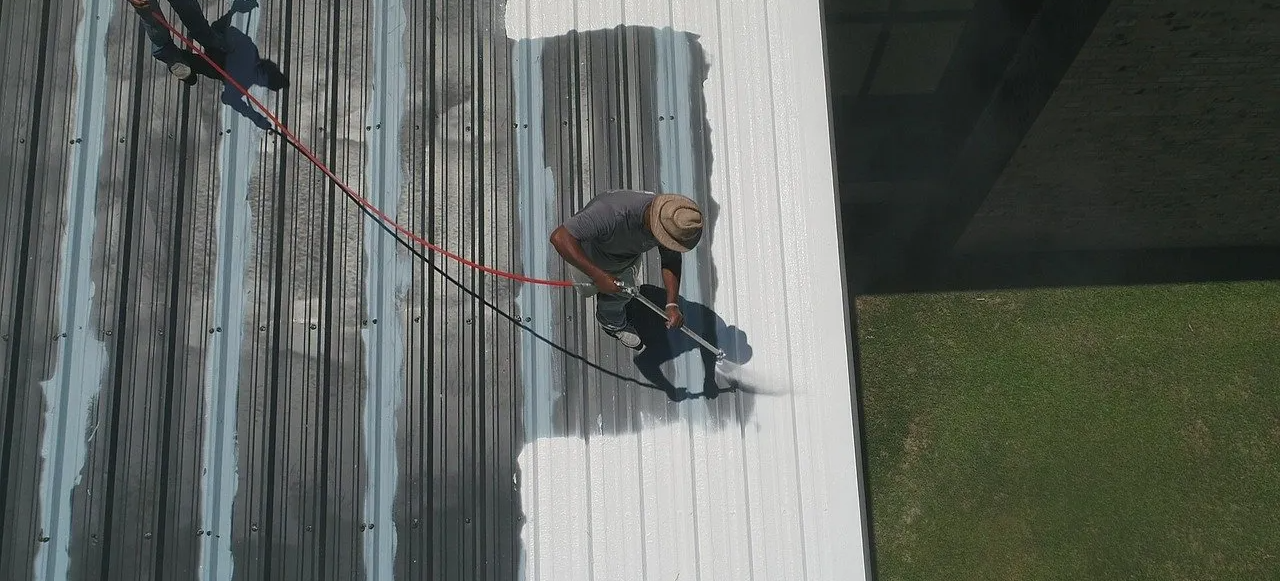 Man on a metal roof spraying a coating to protect the roof