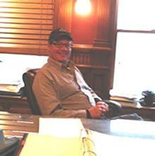 A man is sitting at a desk in front of a window.