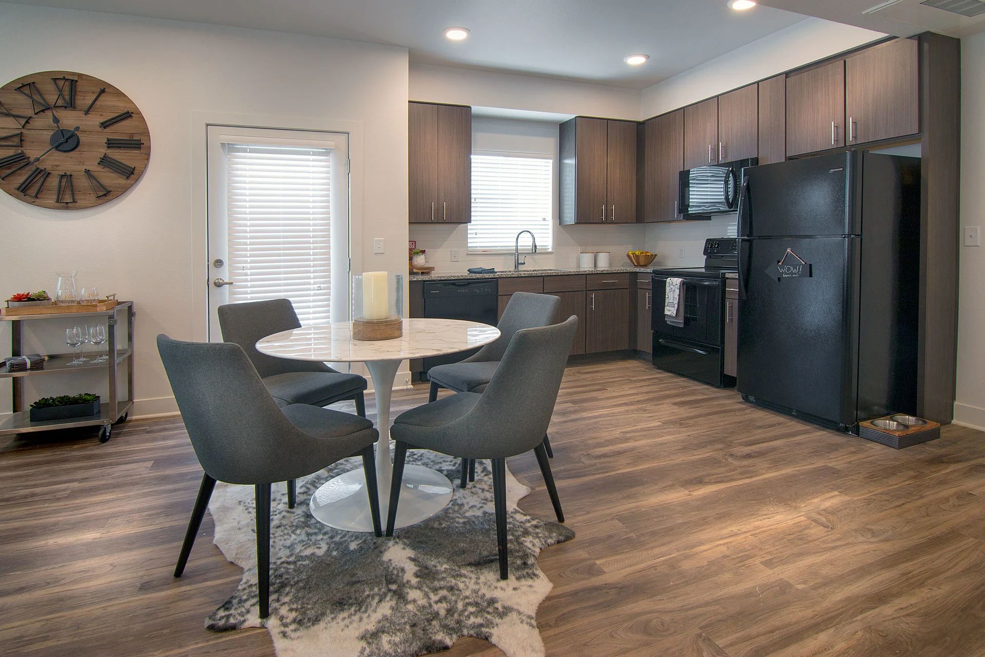 Modern kitchen and dining area with round table, gray chairs, wood cabinets, and black appliances.