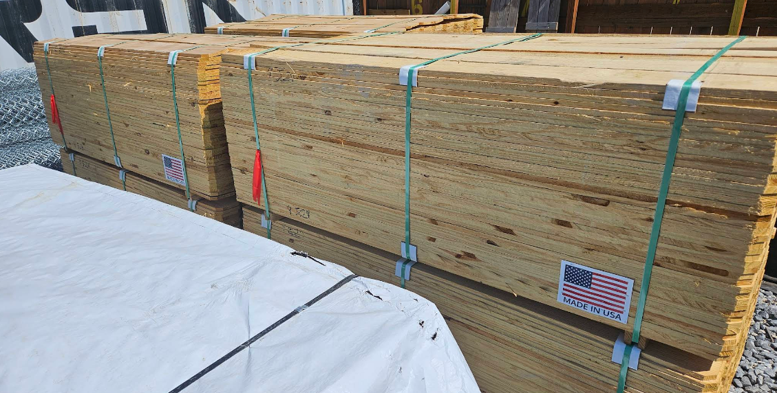 Bundled wooden lumber stacked outdoors, strapped with blue and green bands, with snow in the foreground