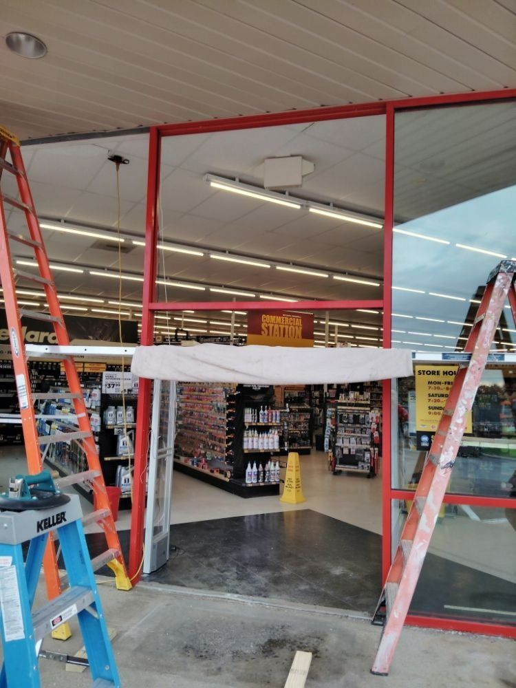Storefront with red frame, glass, and open doorway, ladders on sides. Interior shelves visible.