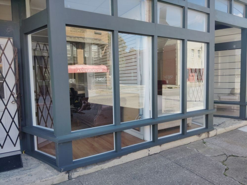 Storefront with large windows reflecting street scene; gray trim, wood floors, and visible interior.