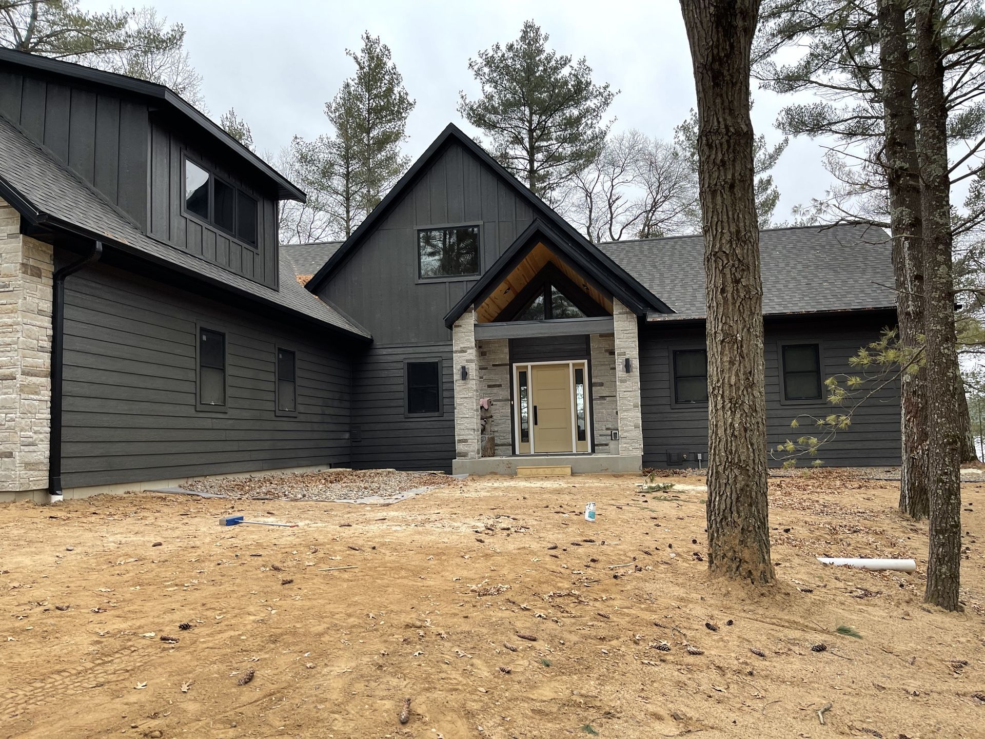 A large black house is sitting in the middle of a field surrounded by trees.