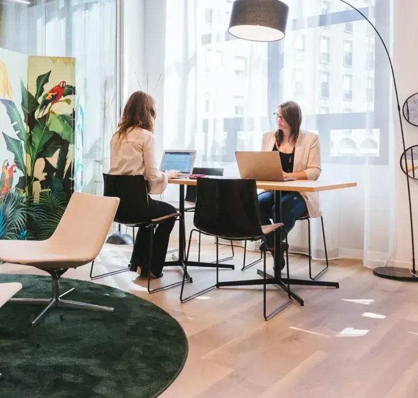 Two women are sitting at a table with laptops.