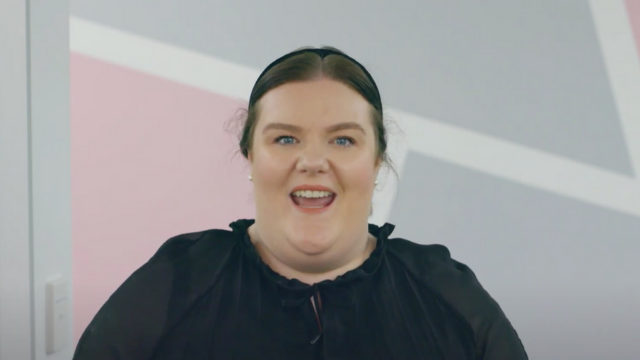A woman in a black shirt is smiling in front of a wall.