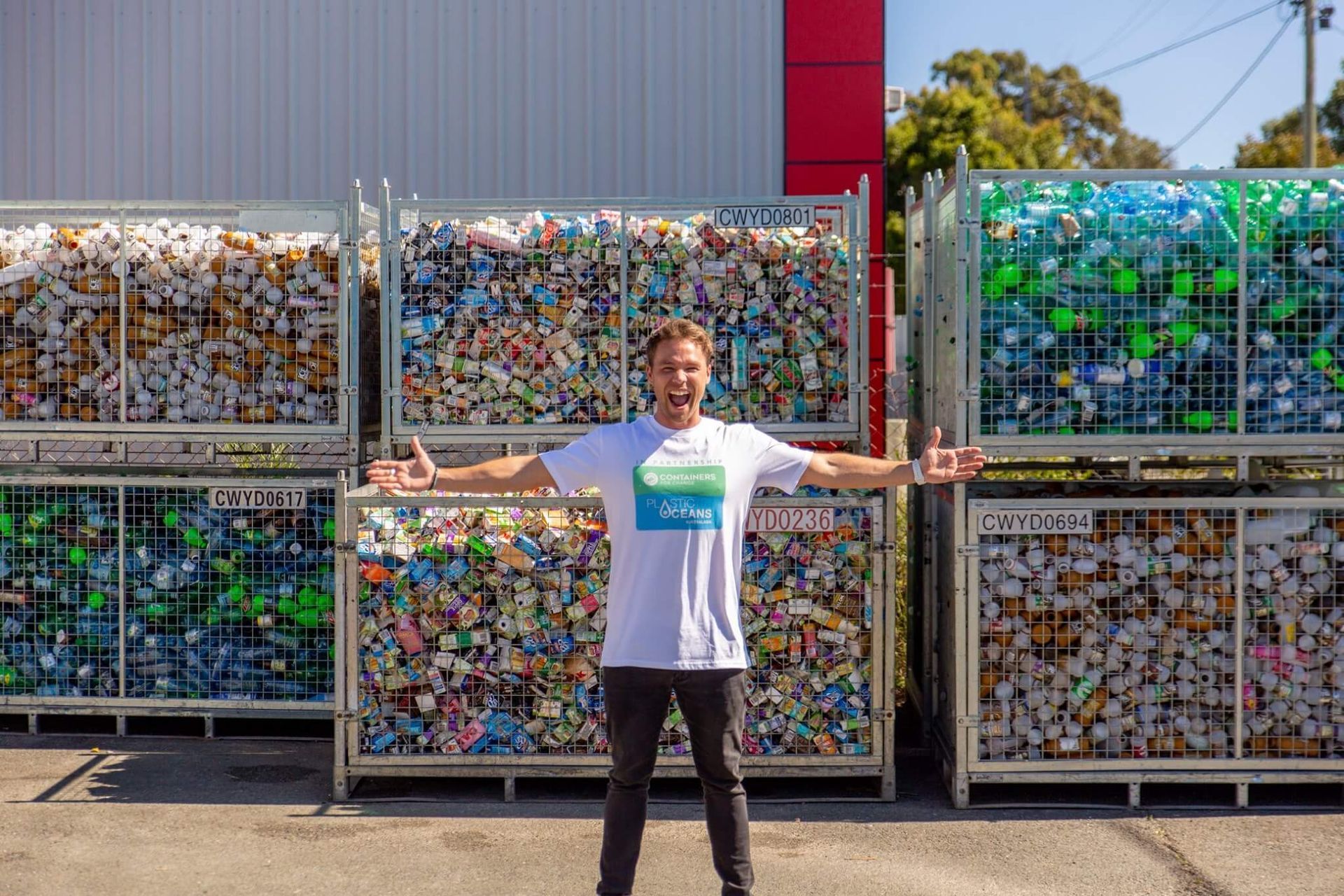 A man is standing in front of a pile of plastic bottles.