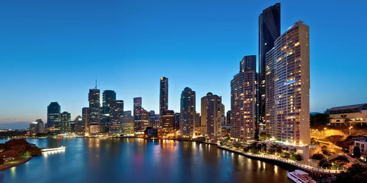 A city skyline at night with a river in the foreground.