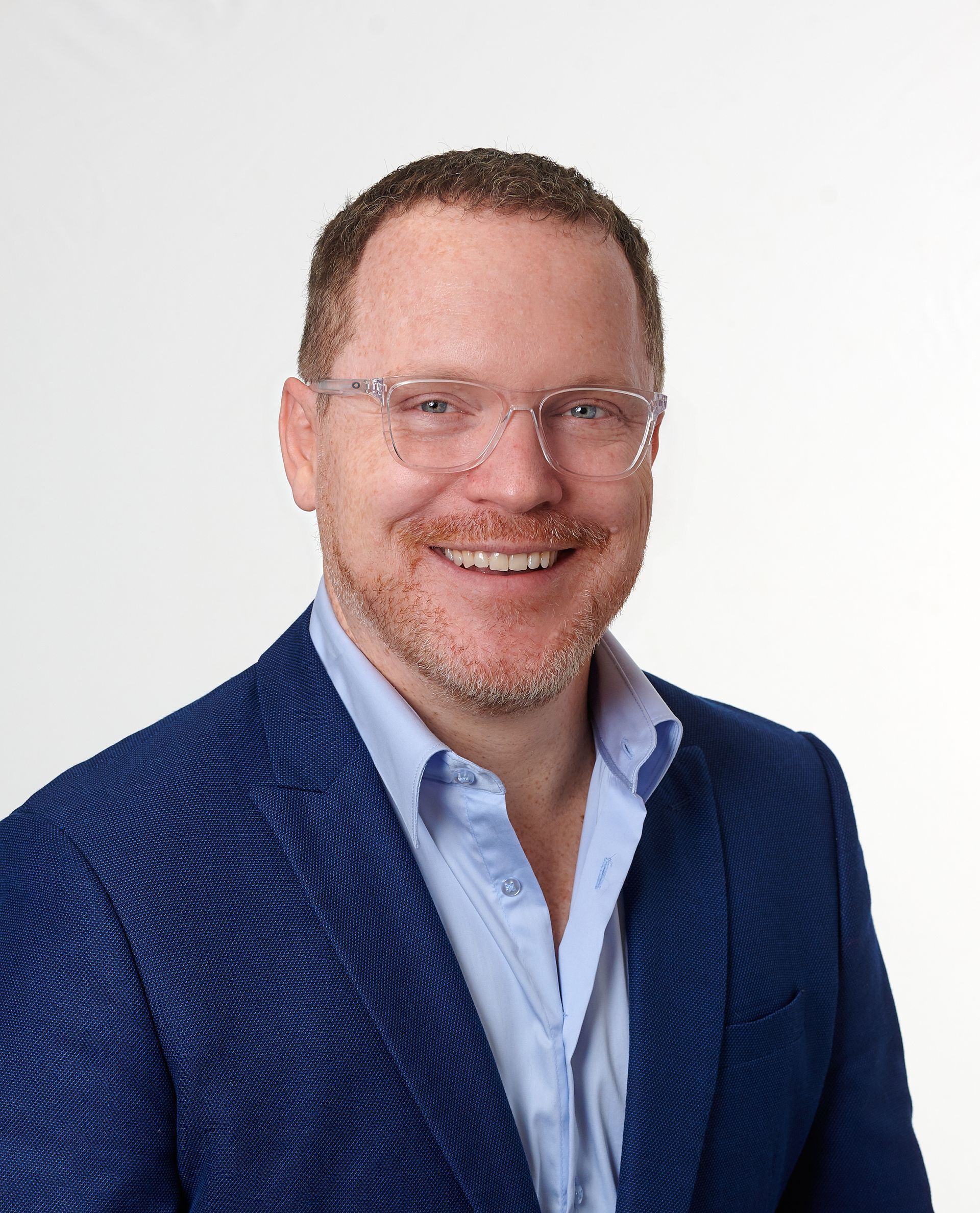 A man wearing glasses and a blue jacket is smiling for the camera.