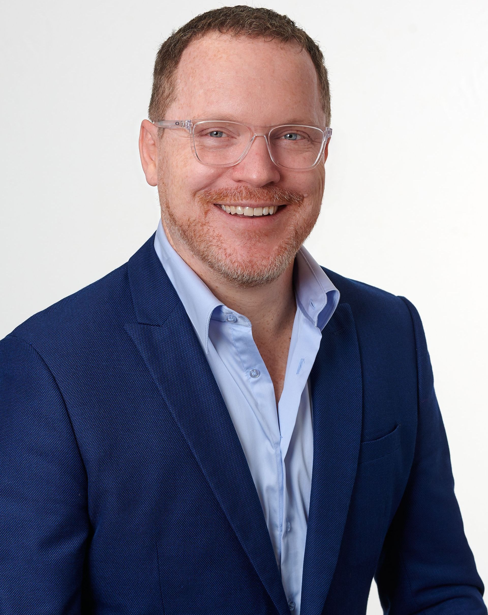 A man wearing a blue suit and glasses is smiling for the camera.