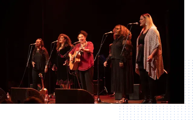 A group of women are singing into microphones on a stage.