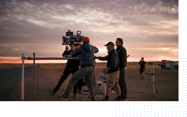 A group of people are standing around a camera in a field.