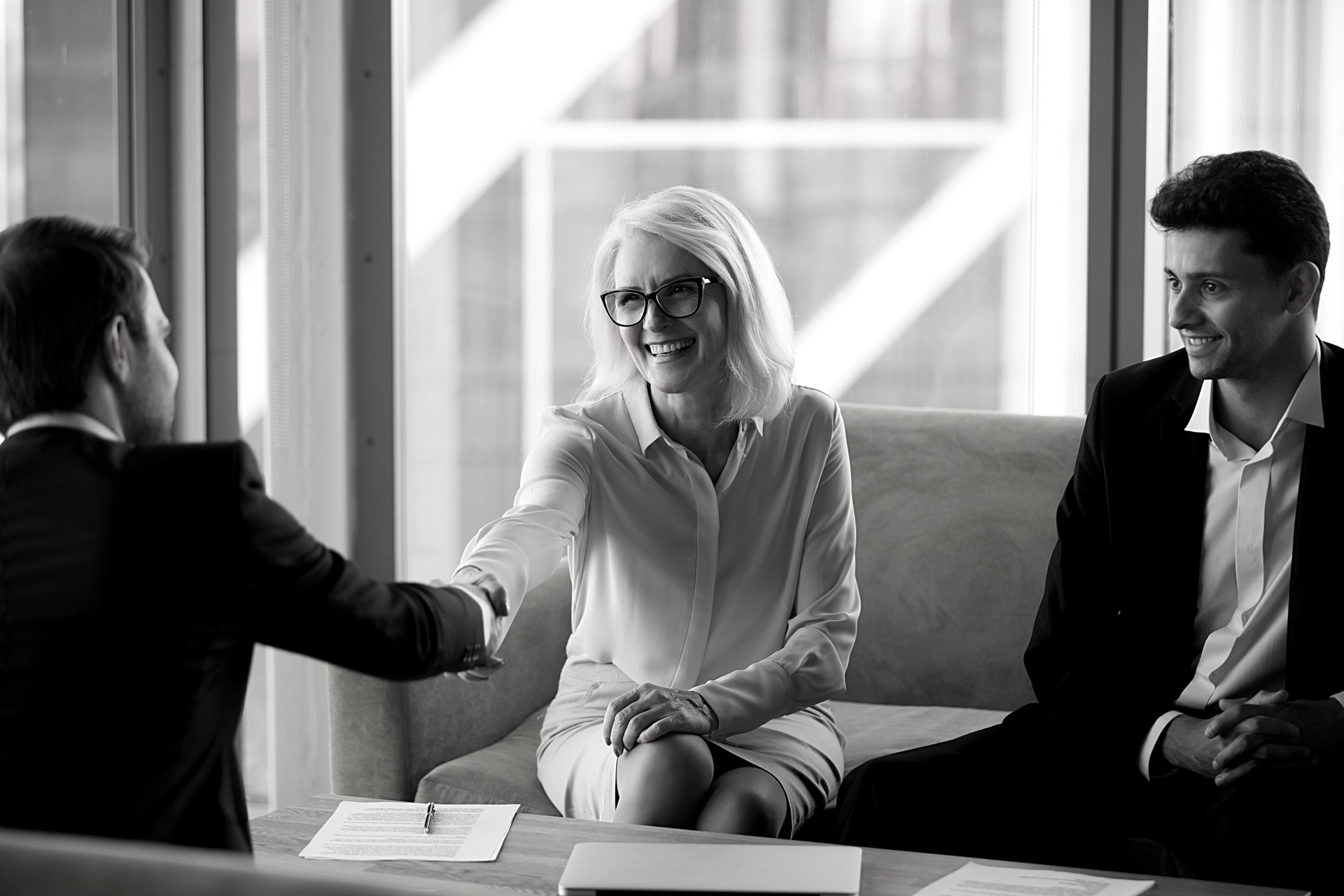 A man and a woman are shaking hands while sitting on a couch.