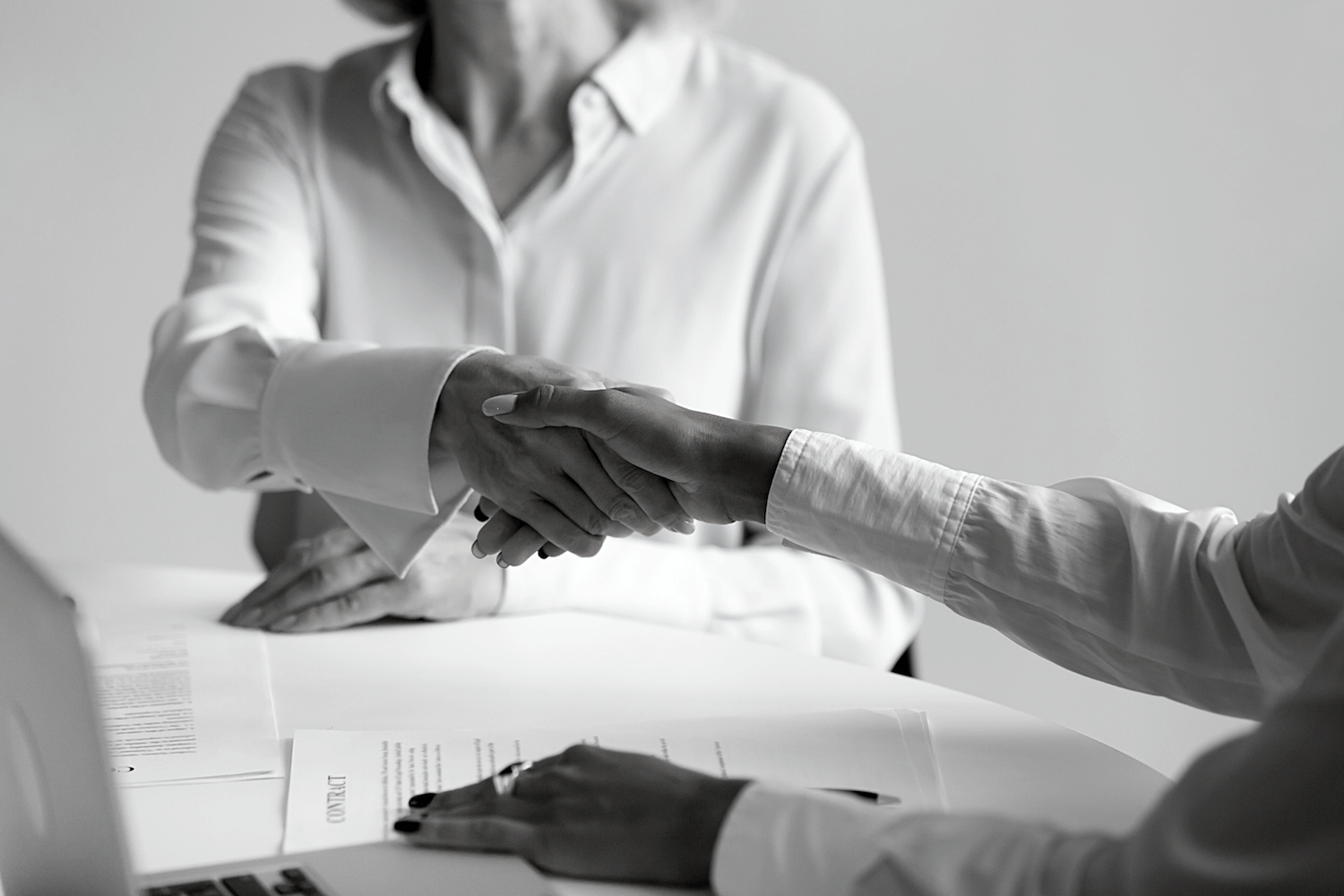 A black and white photo of two people shaking hands over a table.