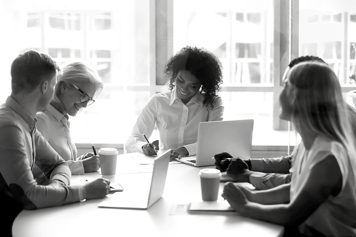 A group of people are sitting around a table with laptops.