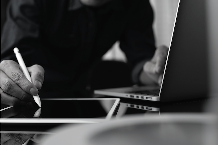 A black and white photo of a person using a tablet and a laptop.
