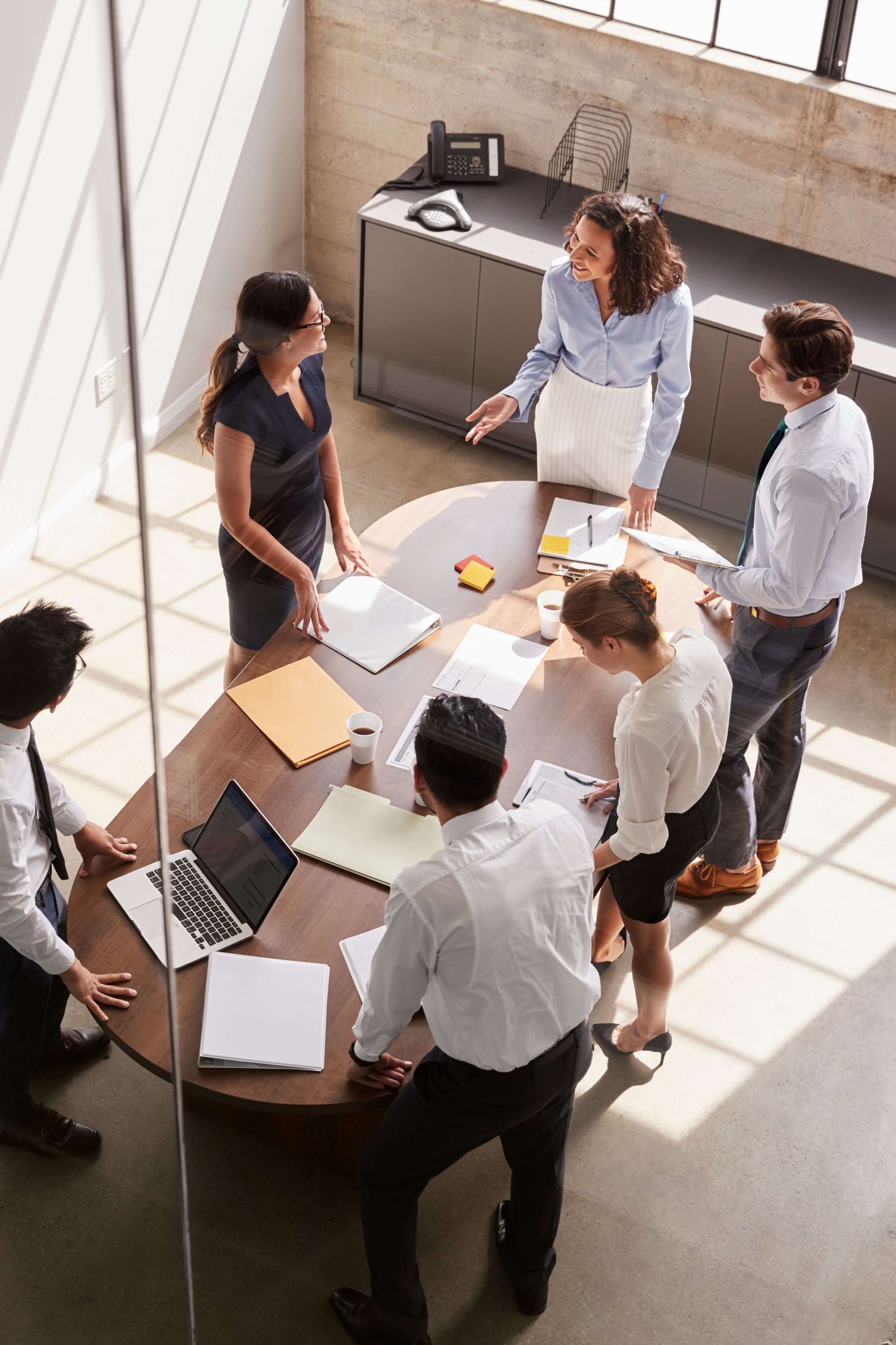 A group of people are sitting around a round table having a meeting.