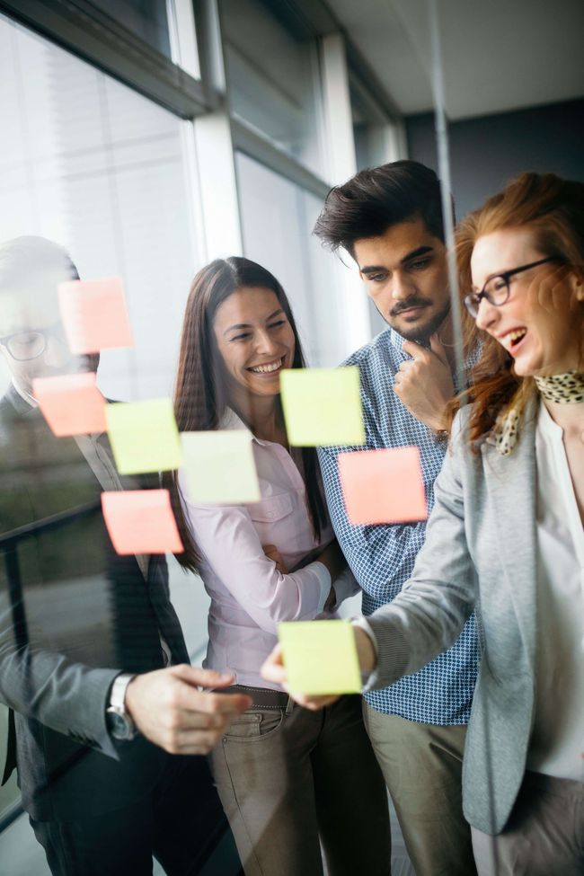 A group of people are looking at sticky notes on a glass wall.