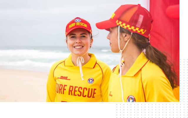 Two women wearing surf rescue uniforms are standing on a beach