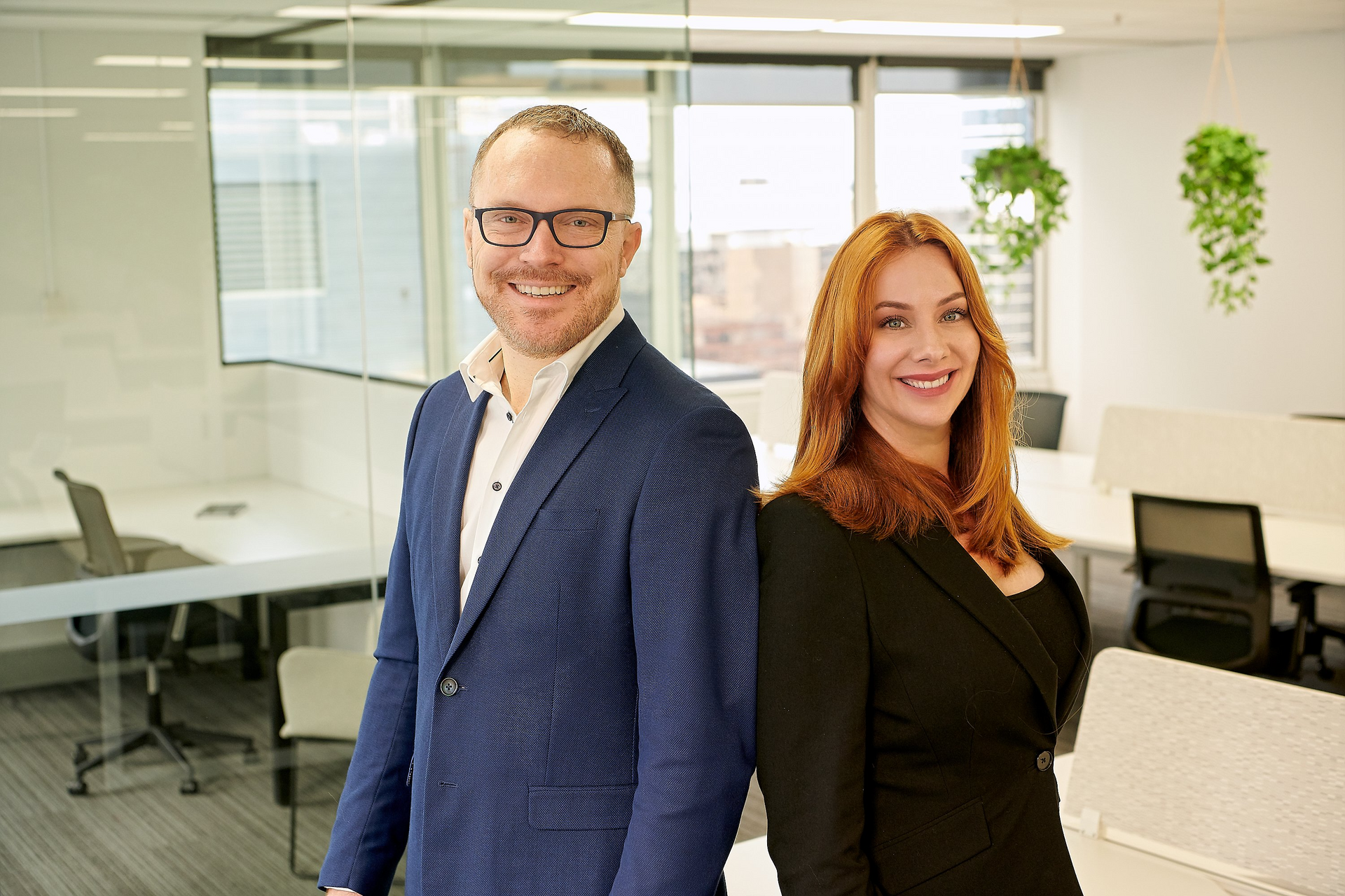 A man and a woman are standing back to back in an office.