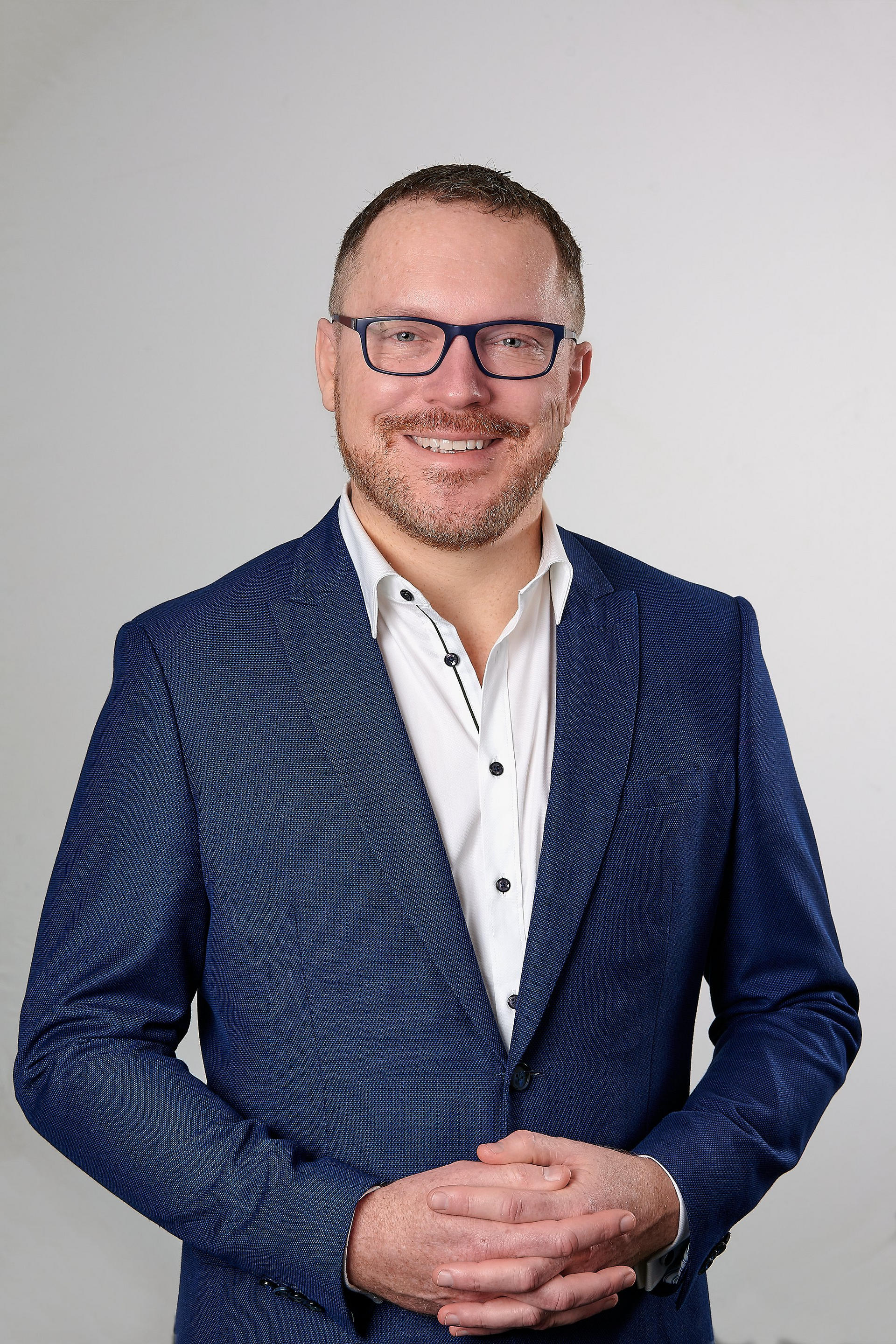 A man wearing a blue jacket and glasses is smiling for the camera.