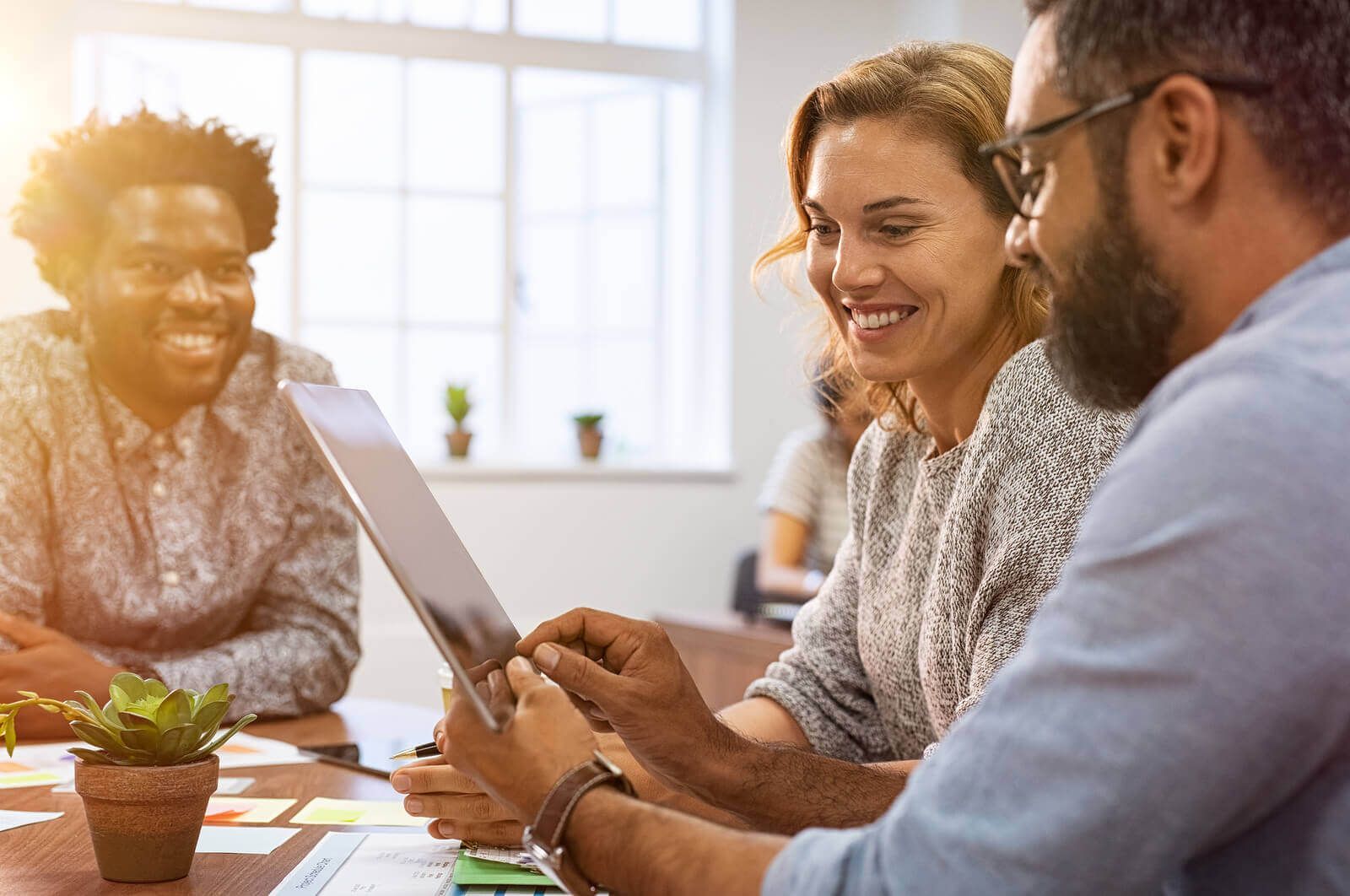 A group of people are sitting around a table looking at a tablet.