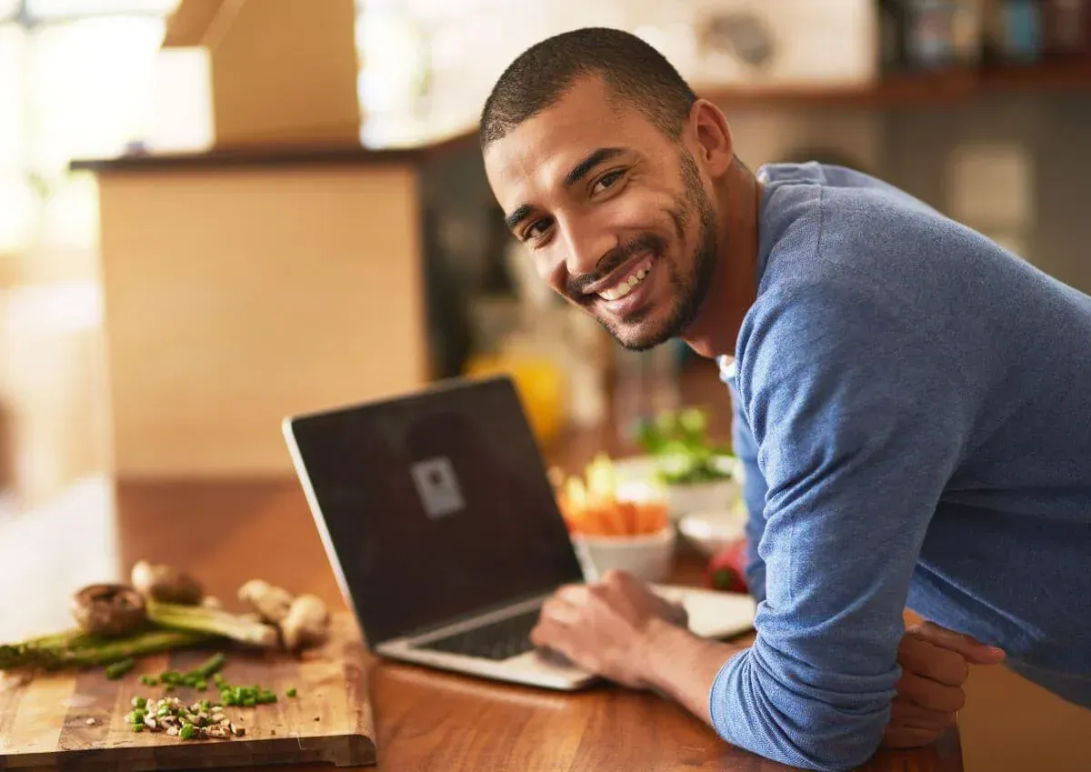 A man is leaning on a counter using a laptop computer.