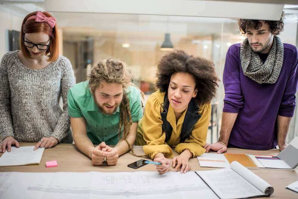 A group of young people are sitting around a table looking at a piece of paper.